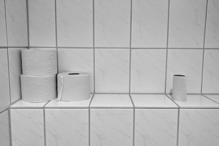White bathroom tiled wall with three rolls of toilet paper sitting on it